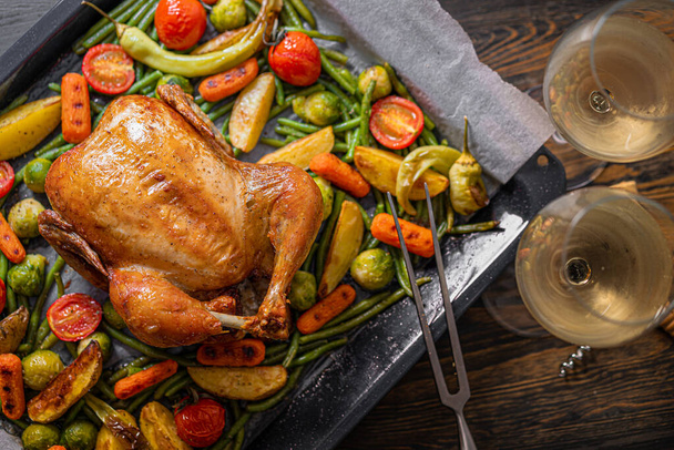 Festive dinner for two of chicken and vegetables. baking sheet with baked chicken and baked green beans, baby carrots, potatoes, green peppers and Brussels sprouts. two glasses of wine. - Foto, Imagen