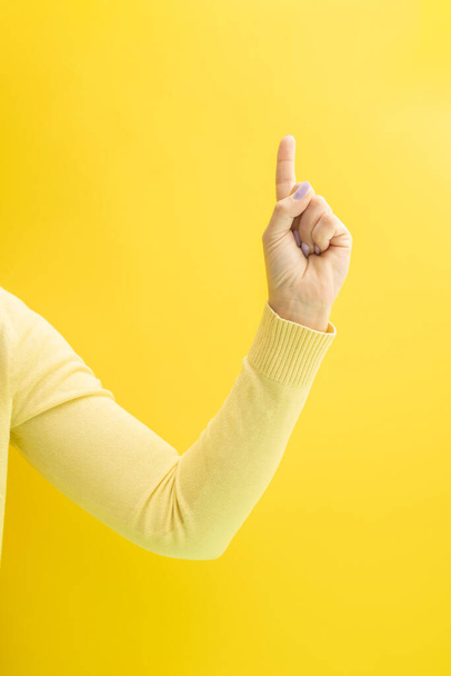 Η γυναίκα με το κίτρινο πουλόβερ δείχνει το δάχτυλό της προς τα πάνω.. - Φωτογραφία, εικόνα