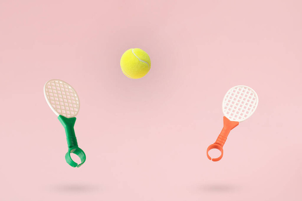 Raquetas de tenis juguetes y una pelota sobre un fondo rosa. - Foto, Imagen