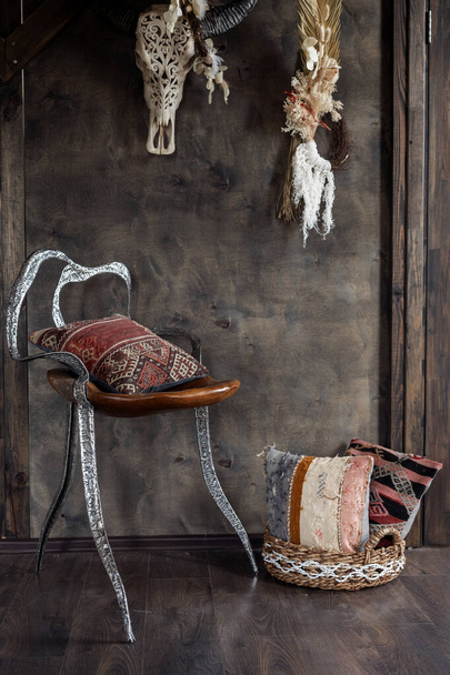 Etnikai párnák fonott kosárban és fából készült székben a szürke falnak támasztva a tetőtéri nappaliban. Függőleges kilátás otthoni dekoráció és kényelmes bútorok a házban vagy bemutatóteremben - Fotó, kép