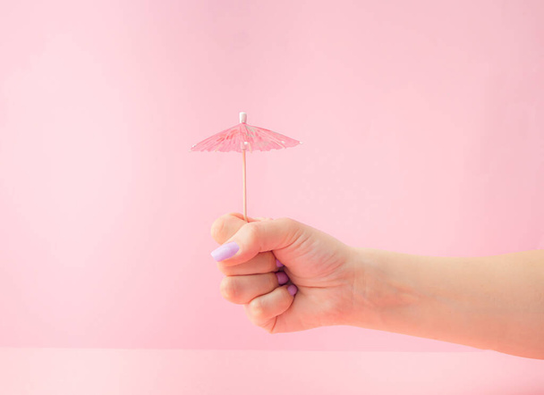 Beautiful female hand, hold ice cream summer beach umbrella on a pink pastel background. - Photo, Image