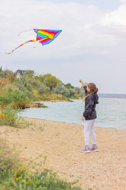 A teenager girl launches a bright multi-colored kite into the sky. concept of outdoor activities and a healthy lifestyle. - Photo, Image