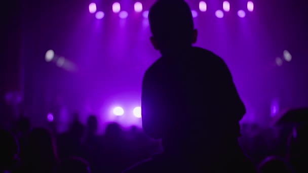 Silhouette Fan Junge auf Vater Schultern genießen Künstler während des Konzerts in der Nacht zu hören, Menschen auf dem Hintergrund der Bühne mit Lichtern in lila Farbe - Filmmaterial, Video