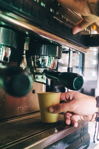 Primo piano di un barista che prepara il caffè. Il processo di fare il cappuccino in una macchina da caffè. Tazza di misura in mano. La bevanda calda viene versata in un bicchiere di carta. Cibo da asporto - Foto, immagini