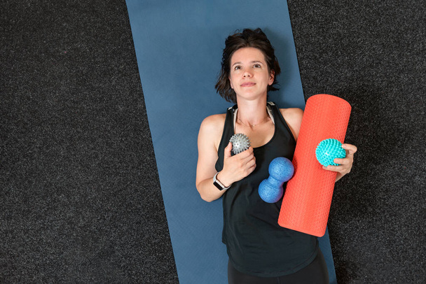 Молода атлетична дівчина лежить на маті йоги з різними міофазними рулонами. Обладнання для МФР. Міофазне звільнення. Краєвид. - Фото, зображення