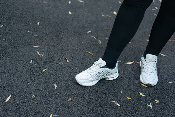 Pies de mujer en zapatillas deportivas contra el fondo de asfalto con hojas de otoño. Deportes al aire libre. - Foto, imagen