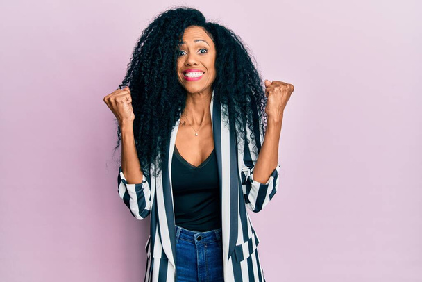 Middle age african american woman wearing casual clothes celebrating surprised and amazed for success with arms raised and open eyes. winner concept.  - Photo, Image