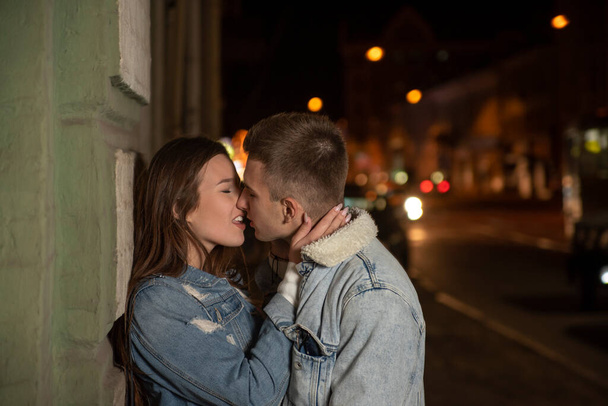 Πορτρέτο των νέων φιλιά ζευγάρι στο φόντο της πόλης νύχτα. Ρομαντικό ραντεβού. νεαρό ζευγάρι ερωτευμένο. Όμορφο κορίτσι αγκαλιάζει τον άντρα. - Φωτογραφία, εικόνα