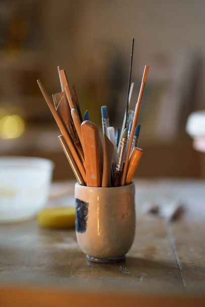 Paintbrush with tools for pottery shaping in bowl on table. Ceramics equipment in creative art space - Fotoğraf, Görsel