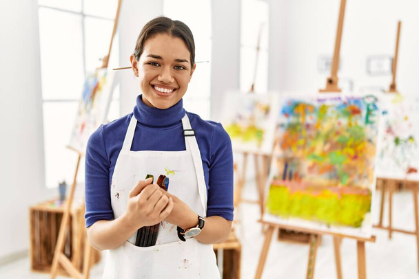 Jeune femme brune au studio d'art avec les mains jointes et les doigts croisés souriant détendu et joyeux. succès et optimisme  - Photo, image