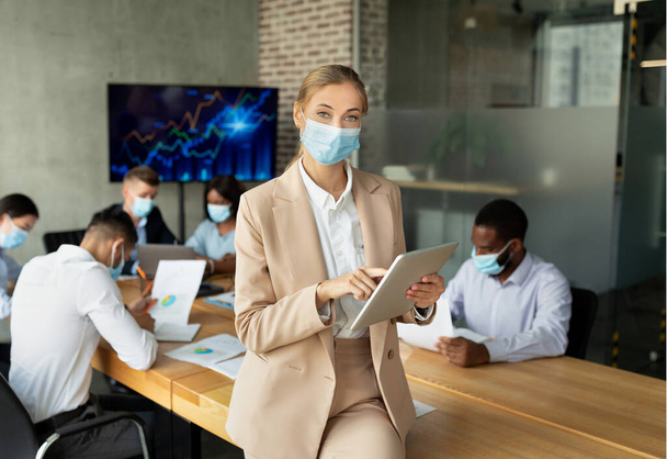 Veiligheid op de werkplek tijdens de pandemie. Jonge zakenvrouw in medische maskers poseren tijdens conferentie vergadering - Foto, afbeelding