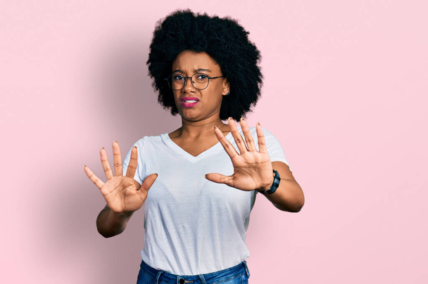 Jeune femme afro-américaine portant un t-shirt blanc décontracté faisant un geste d'arrêt avec les paumes des mains, expression de colère et de frustration  - Photo, image
