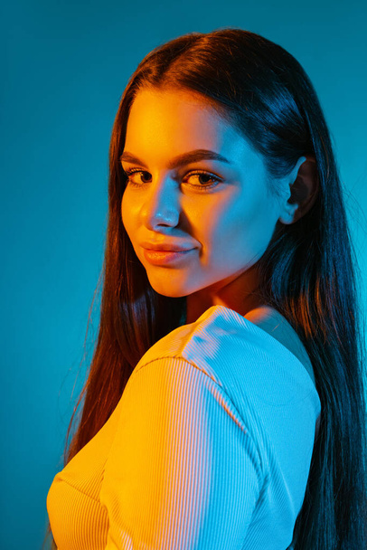 Portrait of young beautiful girl looking at camera, posing isolated over blue background in neon light. Side view - Fotó, kép