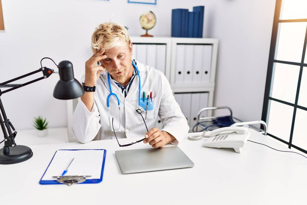 Young caucasian man wearing doctor uniform stressed working at clinic - Fotografie, Obrázek