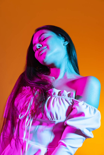Beautiful portrait of atrractive young girl passionately dancing isolated over orange background in neon ligh - Foto, immagini