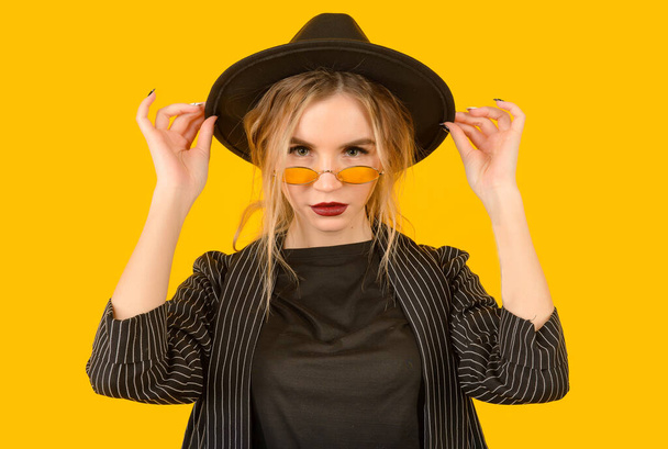 Young girl posing on yellow background half body direct look raising hands brown clothes yellow glasses copy space minimalistic serious - Foto, imagen