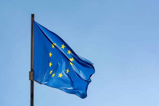 Sininen keltaisilla tähdillä Euroopan unionin lippu heiluttaa lipputangolla ja sinisellä taivaalla - Valokuva, kuva