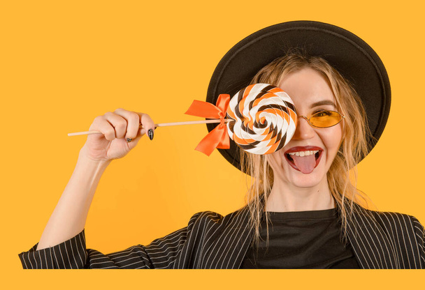 Young girl posing on yellow background with lollipop direct look close up with tongue smiling brown clothes yellow glasses copy space minimalistic - Фото, зображення