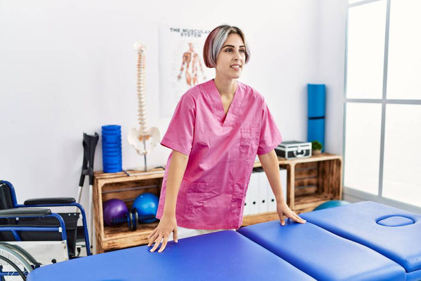 Jonge Kaukasische fysiotherapeut glimlachend gelukkig staande in de kliniek. - Foto, afbeelding