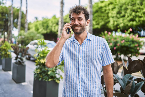 Joven hombre hispano sonriendo feliz hablando en el smartphone de la ciudad. - Foto, imagen