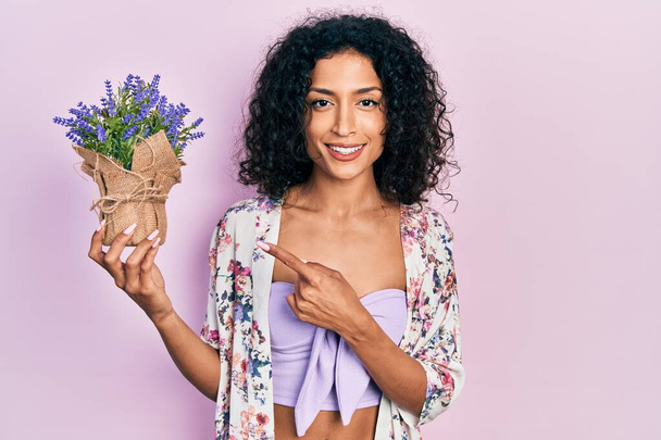 Nuori latino tyttö tilalla laventeli kasvi hymyillen onnellinen osoittaa käsi ja sormi  - Valokuva, kuva