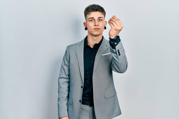 Joven chico caucásico con dilatación de orejas usando chaqueta de negocios haciendo gesto italiano con la mano y los dedos expresión confiada  - Foto, Imagen