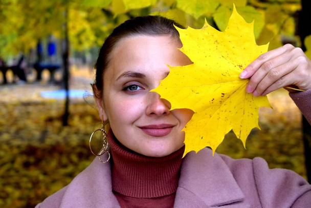 Meisje in een jas in een herfstpark op een achtergrond van gele bladeren - Foto, afbeelding