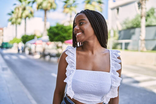 Młoda afrykańska dziewczyna uśmiecha się szczęśliwa stojąc w mieście. - Zdjęcie, obraz