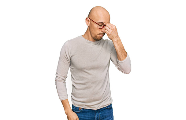 Bald man with beard wearing casual clothes and glasses tired rubbing nose and eyes feeling fatigue and headache. stress and frustration concept.  - Photo, Image