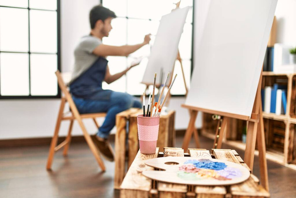 Giovane artista ispanico uomo sorridente pittura felice a studio d'arte. - Foto, immagini
