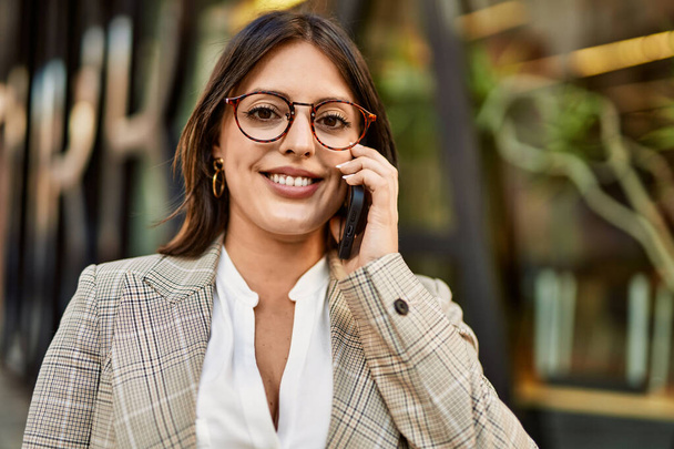 Junge hispanische Geschäftsfrau lächelt glücklich mit dem Smartphone in der Stadt. - Foto, Bild