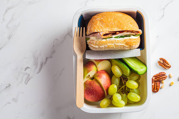 Healthy office food concept. Balanced food in lunch box - turkey sandwich and fruits, top view, white background. - Foto, Imagem