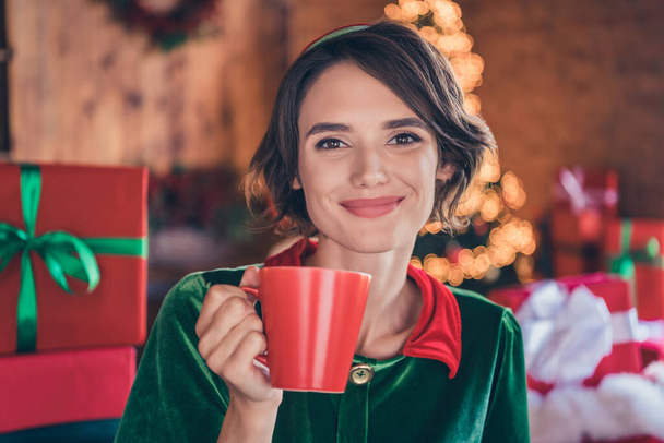 Foto positiver fröhlicher Dame halten Tasse trinken Kakao genießen Sie Weihnachten tragen Elfenkostüm in dekorierten Büro drinnen - Foto, Bild