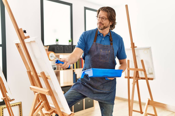 Moyen Age caucasien homme souriant dessin confiant à l'aide de rouleau de peinture au studio d'art - Photo, image