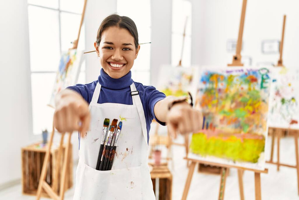 Giovane donna bruna in studio d'arte che indica te e la fotocamera con le dita, sorridendo positivo e allegro  - Foto, immagini