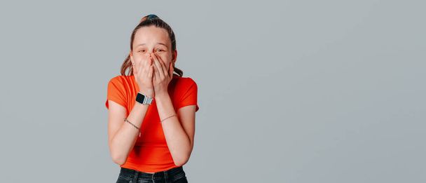 Excited beautiful brunette teen girl covered her mouth with her hands, hear amazing good news, hear fantastic announcement, standing on gray background. Copy space for your text - Valokuva, kuva