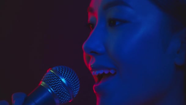 Επαγγελματίας τραγουδιστής. Πορτρέτο της νεαρής εμπνευσμένης Ασιάτισσας που τραγουδάει όμορφο τραγούδι σε μικρόφωνο σε μωβ νέον φώτα - Πλάνα, βίντεο