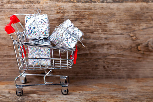 Shopping cart with Christmas gifts on a wooden background. Holiday sale. - Fotografie, Obrázek
