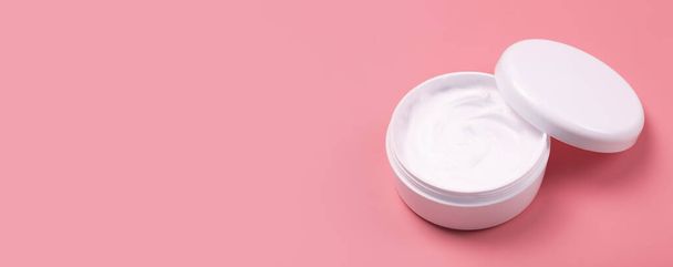 Cosmetic cream banner background. White cosmetic cream for skin and body in an open white jar on a pink empty background. Copy space - Foto, Imagen