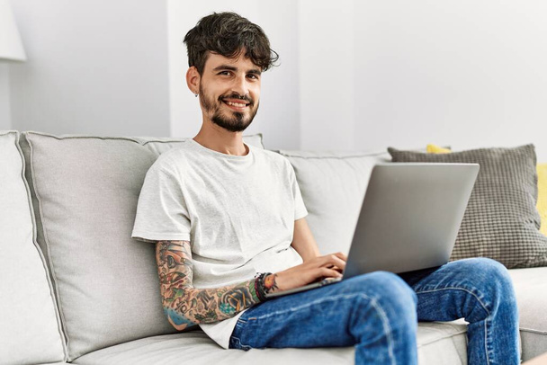 Young hispanic man using laptop sitting on the sofa at home. - Foto, Imagen