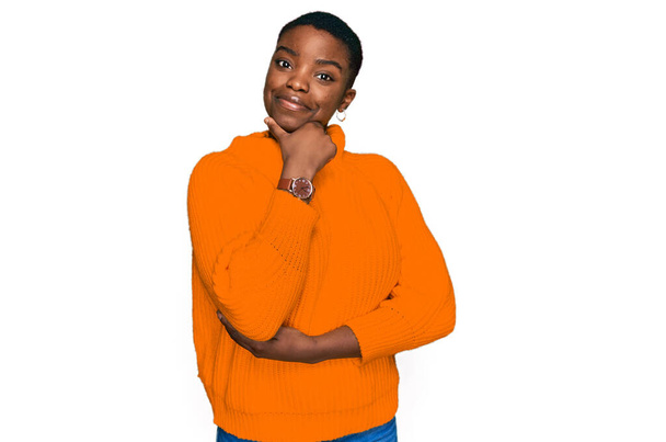 Молодая африканская американка в повседневной одежде с рукой на подбородке думает о вопросе, задумчивом выражении лица. улыбаясь с вдумчивым лицом. Концепция сомнений.  - Фото, изображение
