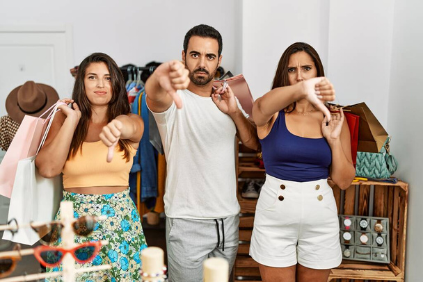 Ryhmä nuoria latino ihmiset tilalla ostoskassit klo vaatekauppa vihainen kasvot, negatiivinen merkki osoittaa vastenmielisyyttä peukalot alas, hylkääminen käsite  - Valokuva, kuva
