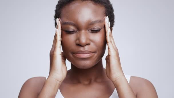 Concepto de dolor de cabeza. Joven mujer afroamericana hermosa que sufre de migraña, masajeando sus templos - Imágenes, Vídeo