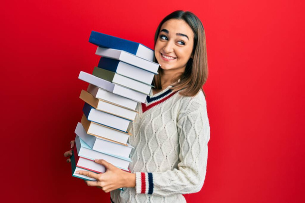 Mladá brunetka studentka drží hromadu knih, usmívá se a dívá se stranou a přemýšlí.  - Fotografie, Obrázek
