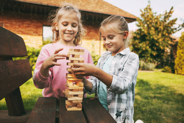 Две девушки веселятся и играют в деревянные настольные игры на открытом воздухе рядом с их домом. - Фото, изображение