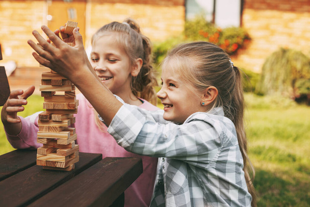 Δύο κορίτσια διασκεδάζουν και παίζουν ένα ξύλινο επιτραπέζιο παιχνίδι σε εξωτερικούς χώρους κοντά στο σπίτι τους. - Φωτογραφία, εικόνα