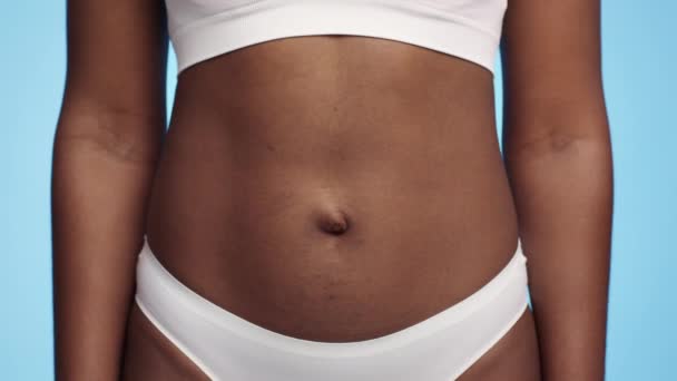 Σωματική αντίληψη. Κοντινό πλάνο της αφρικανικής αμερικανικής γυναικείας κοιλιάς με ραγάδες που θέτουν πάνω από το μπλε φόντο στούντιο - Πλάνα, βίντεο