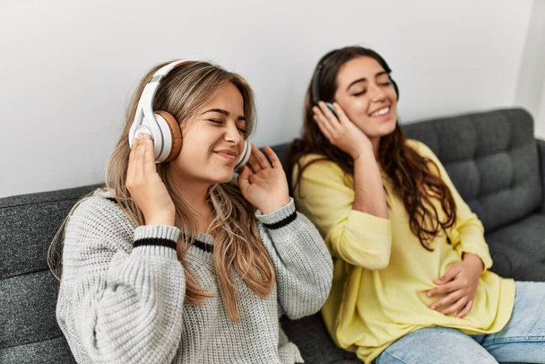 Młoda para uśmiechnięta szczęśliwa słuchając muzyki siedzącej na kanapie w domu. - Zdjęcie, obraz