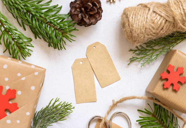 Vánoční papírová dárková etiketa na bílém stole s jedlovými větvemi, zabalené dárky a vánoční ozdoby horní pohled. Rustikální zimní kompozice s prázdnou dárkovou značkou Mockup, kopírovací prostor - Fotografie, Obrázek