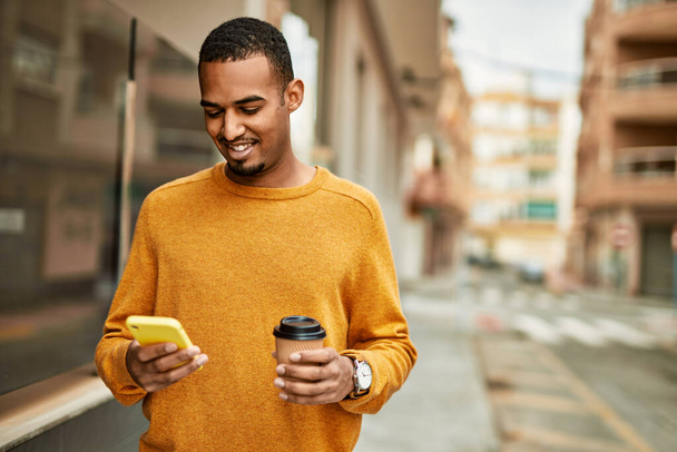 Joven afroamericano usando smartphone bebiendo café en la ciudad. - Foto, imagen